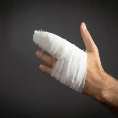 Dłoń z zabandażowanym palcem po urazie. Wygląda na to, że to był wybity palec, który wymagał opatrunku.