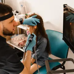 Lekarz wykonuje endoskopię laryngologiczną u dziecka, badając ucho za pomocą endoskopu. Obraz z kamery widoczny na monitorze.