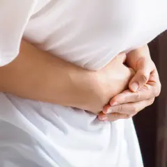 Osoba trzyma się za brzuch, odczuwając ból po lewej stronie.