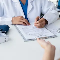 Lekarz notuje objaw kliniczny pacjenta, obok leży stetoskop i ciśnieniomierz.