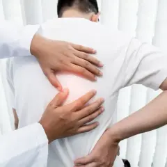 Lekarz bada pacjenta z bólem pod łopatką. Dłonie terapeuty delikatnie uciskają plecy, szukając źródła dyskomfortu.