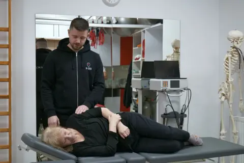 Fizjoterapeuta pomaga pacjentce z bólem kręgosłupa, wykonując delikatny masaż.