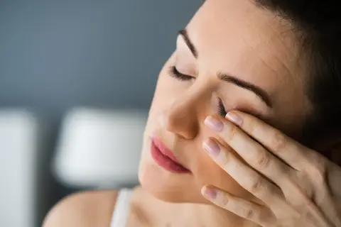 Kobieta zamyka oczy, pocierając je palcami. Czuje silny ból oka, być może od zmęczenia lub podrażnienia.