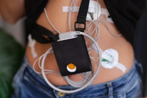 Holter jak się ubrać? Pacjent w dżinsach i czarnej koszulce z przyczepionym urządzeniem monitorującym.