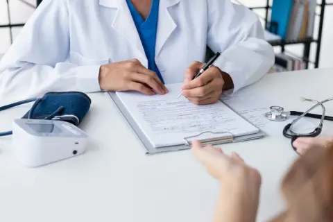 Lekarz notuje objaw kliniczny pacjenta, obok leży stetoskop i ciśnieniomierz.