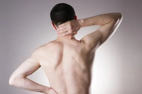 Mężczyzna z bólem karku i pleców, objawy stenozy kanału kręgowego.