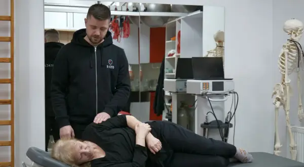 Fizjoterapeuta pomaga pacjentce z bólem kręgosłupa, wykonując delikatny masaż.