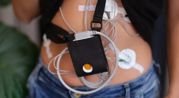 Holter jak się ubrać? Pacjent w dżinsach i czarnej koszulce z przyczepionym urządzeniem monitorującym.