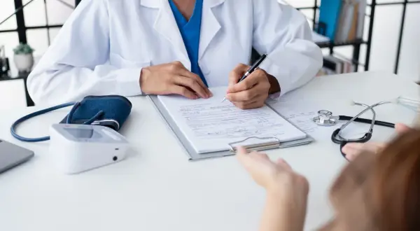 Lekarz notuje objaw kliniczny pacjenta, obok leży stetoskop i ciśnieniomierz.