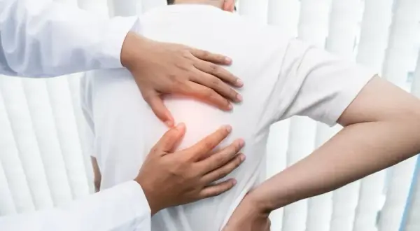 Lekarz bada pacjenta z bólem pod łopatką. Dłonie terapeuty delikatnie uciskają plecy, szukając źródła dyskomfortu.