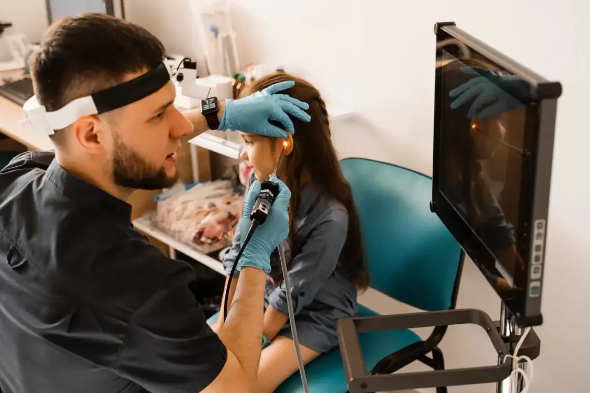 Lekarz wykonuje endoskopię laryngologiczną u dziecka, badając ucho za pomocą endoskopu. Obraz z kamery widoczny na monitorze.