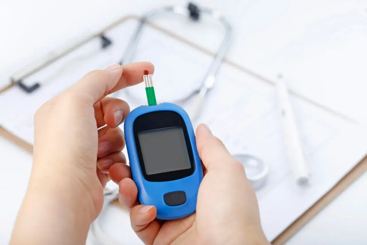 Badanie hba1c co to za badanie? Dłoń z kroplą krwi na pasku glukometru, obok stetoskop i dokumentacja medyczna.