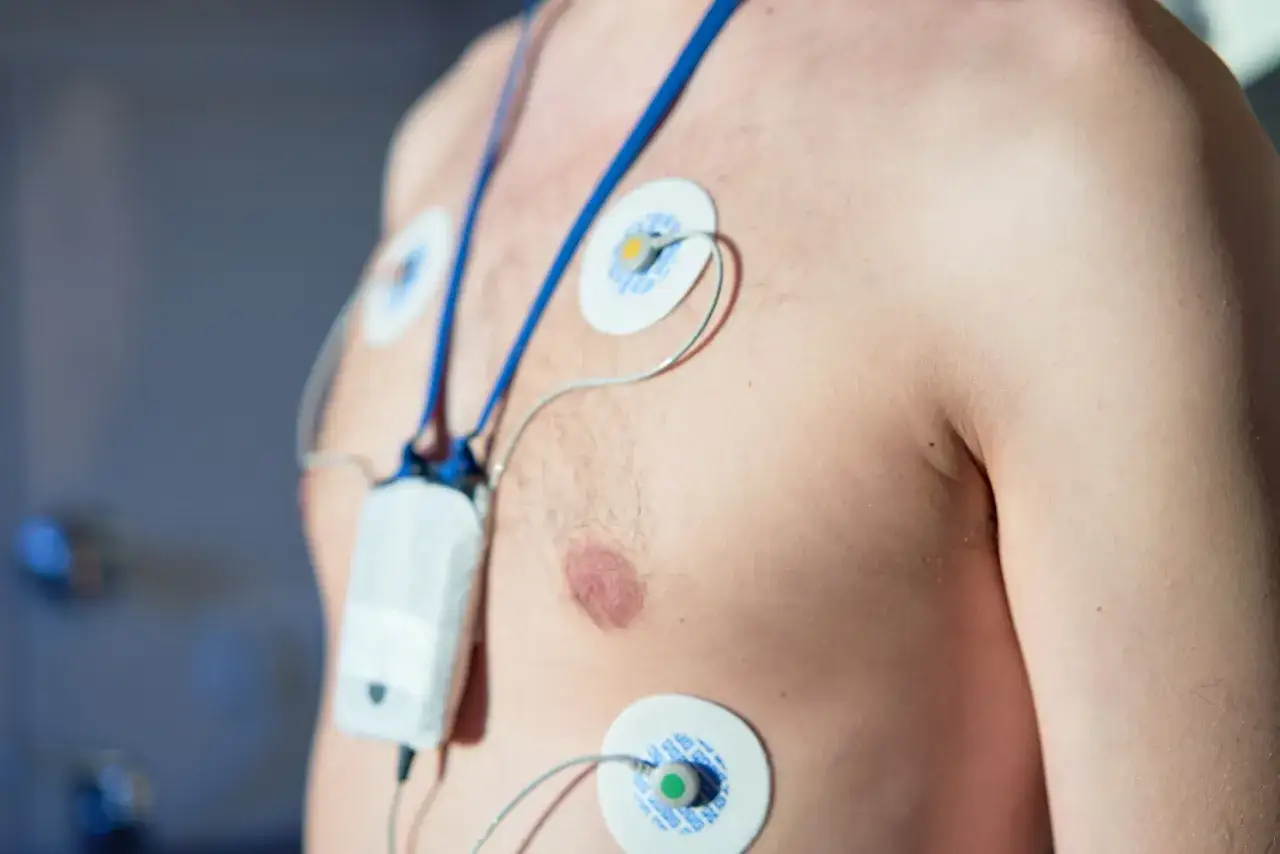 Mężczyzna z przyklejonymi elektrodami do klatki piersiowej, podłączonymi do urządzenia monitorującego. Jak się ubrać do holtera? Luźne ubrania ułatwią założenie i noszenie.