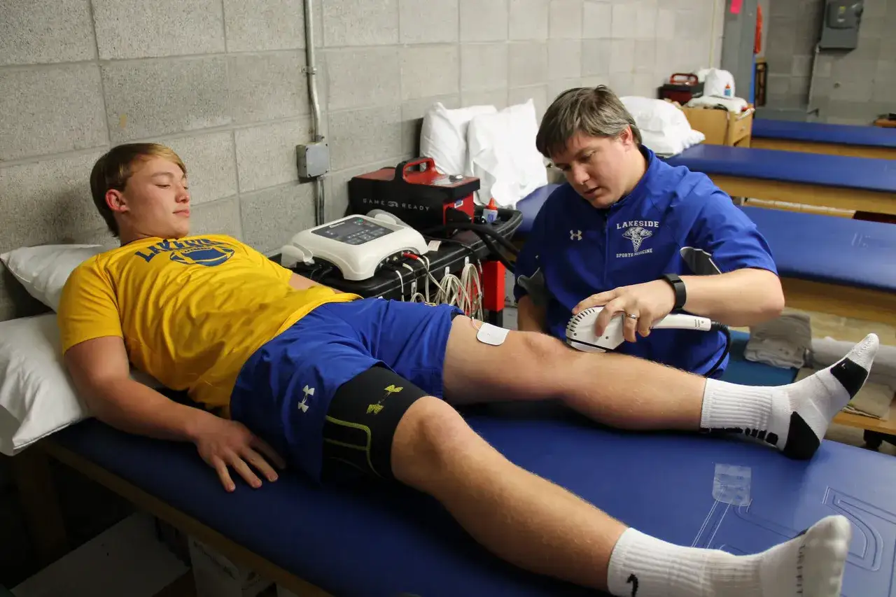 Fizjoterapeuta stosuje terapię ultradźwiękami na kolano młodego sportowca, by złagodzić objawy Osgood-Schlattera.