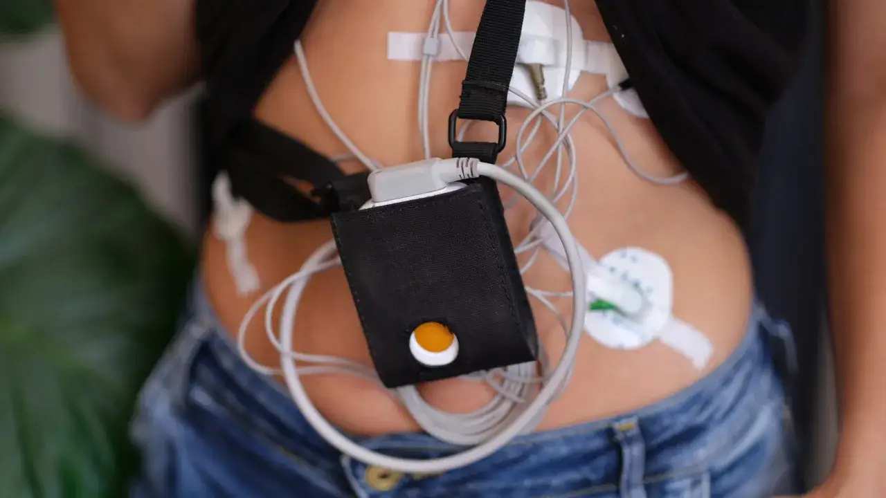 Holter jak się ubrać? Pacjent w dżinsach i czarnej koszulce z przyczepionymi elektrodami i rejestratorem.