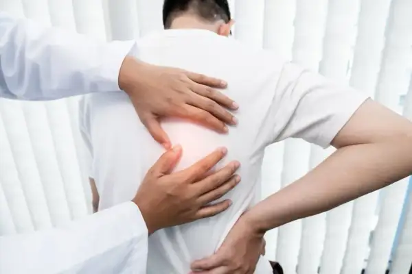 Lekarz bada pacjenta z bólem pod łopatką. Dłonie terapeuty delikatnie uciskają plecy, szukając źródła dyskomfortu.
